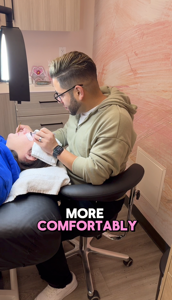 Lash artist working over a client from a saddle stool