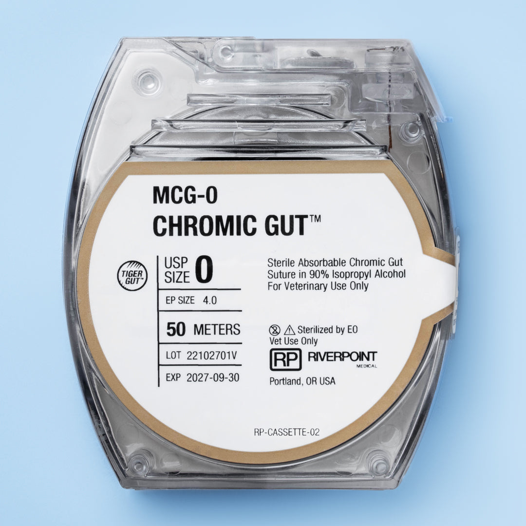 Image of RIVERPOINT's MCG-0 Chromic Gut suture in a clear, round cassette, showcasing a 50-meter length of violet-colored suture. The label indicates size 0, sterilization by gamma irradiation, and key features like superior knot security and smooth surface. The packaging is designed for veterinary use, highlighting the suture's optimized collagen purity and chromium salt treatment for predictable strength and absorption.